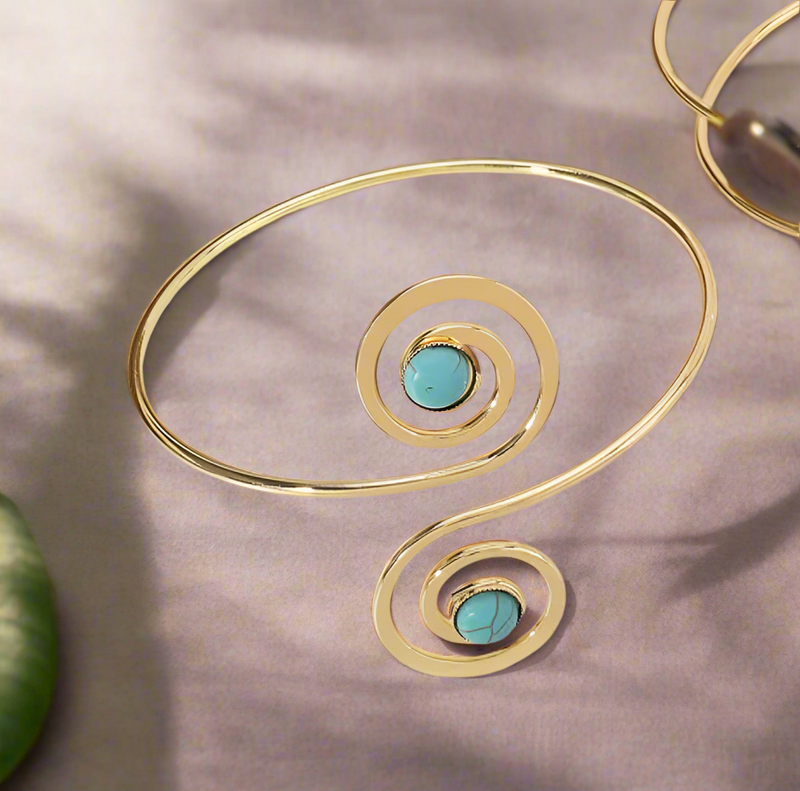 Gold spiral arm cuff bracelet with turquoise stones styled on a woman’s upper arm, combining boho-chic and Afrocentric elegance.