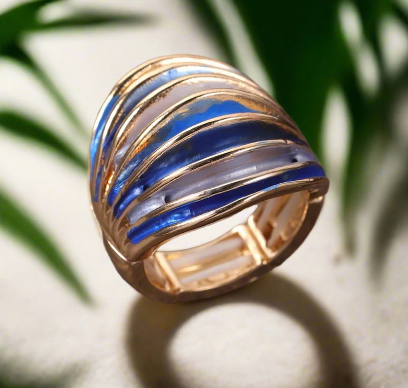 Bold gold statement ring with curved blue and pearl-toned enamel accents, placed on a wooden surface.