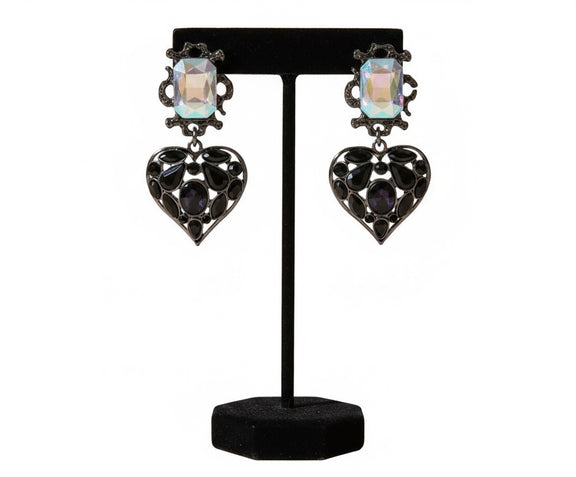 Black heart-shaped statement earrings with iridescent crystal tops, placed on a neutral stone background. Elegant jewelry from Women Are Rubies.
