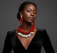 Woman wearing a black dress with a red and white necklace and earrings on a dark background