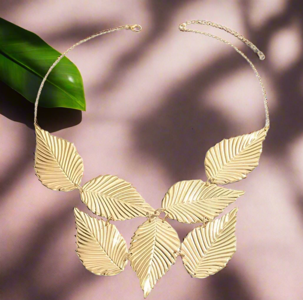 Close-up of the Gladys Golden Leaves Necklace featuring seven large, textured gold leaves arranged in a fan shape on a gold chain, displayed on a neutral background