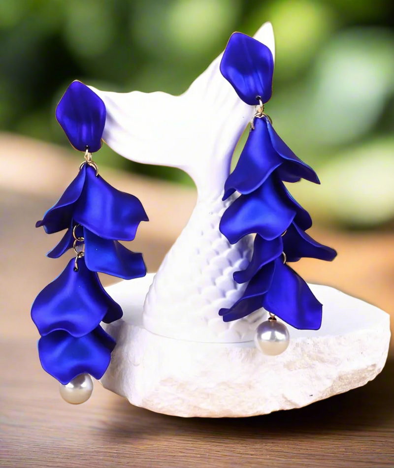 Elegant long drop earring featuring layered royal blue polymer clay petals and a pearl bead at the bottom, worn on a model with blonde hair.
