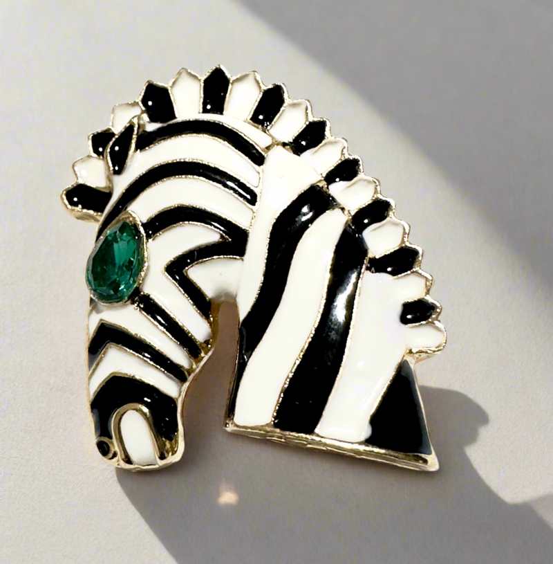 Elegant enamel zebra brooch with black and white stripes, gold-plated details, and a striking emerald-green gemstone eye, perfect for adding a touch of luxury and boldness to any outfit.