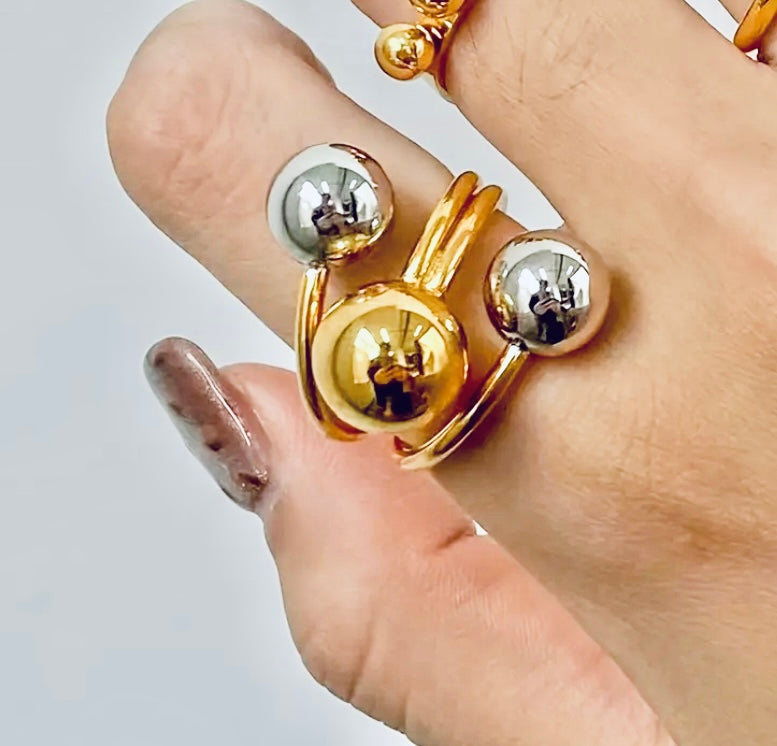 Gold and silver orbit-style statement ring with three polished spheres on a wrap band