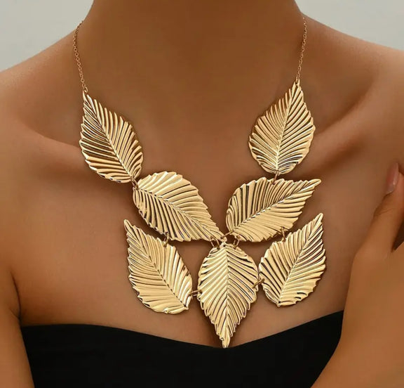 Close-up of the Gladys Golden Leaves Necklace featuring seven large, textured gold leaves arranged in a fan shape on a gold chain, displayed on a neutral background