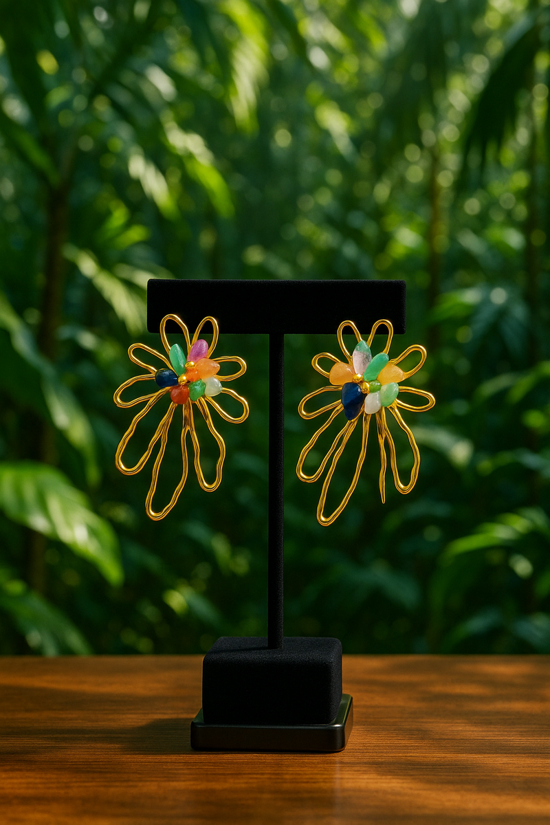 A pair of gold floral statement earrings with open petal design, accented by colorful natural gemstones including green, blue, orange, and purple tones, displayed on a neutral backgroun