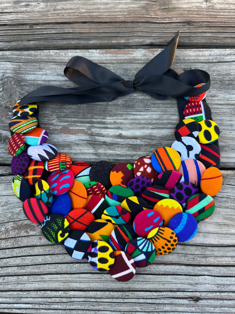 Colorful African print button necklace with satin ribbon tie, laid on rustic wood background.
