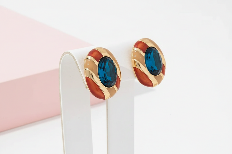 Gold earrings with blue gemstones on a white stand against a light pink background