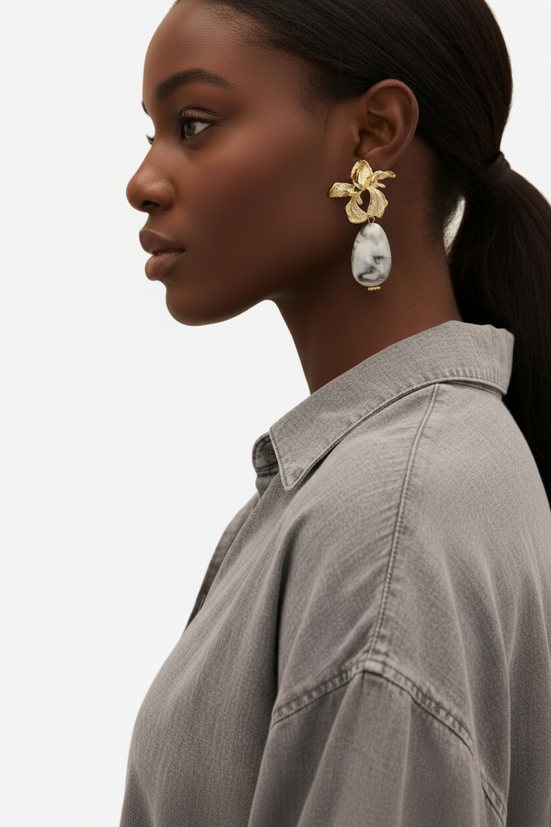 Gold floral drop earrings with white marble teardrop stones on a neutral background.
