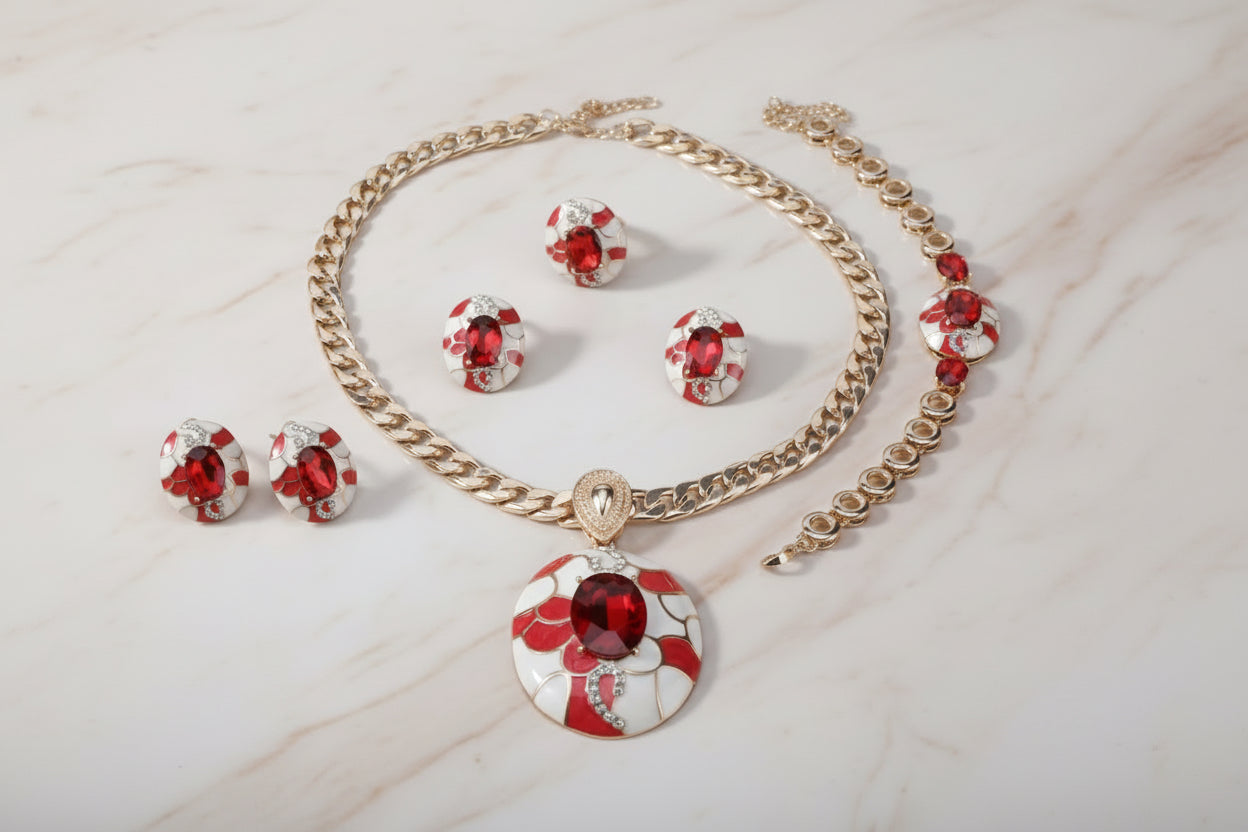Bold red and gold 4-piece celebrity-style jewelry set displayed on a black stand, featuring a chunky gold chain necklace with a large oval red gemstone pendant, matching red gemstone earrings, a coordinating bracelet, and a statement ring, all designed with a glamorous high-fashion look.