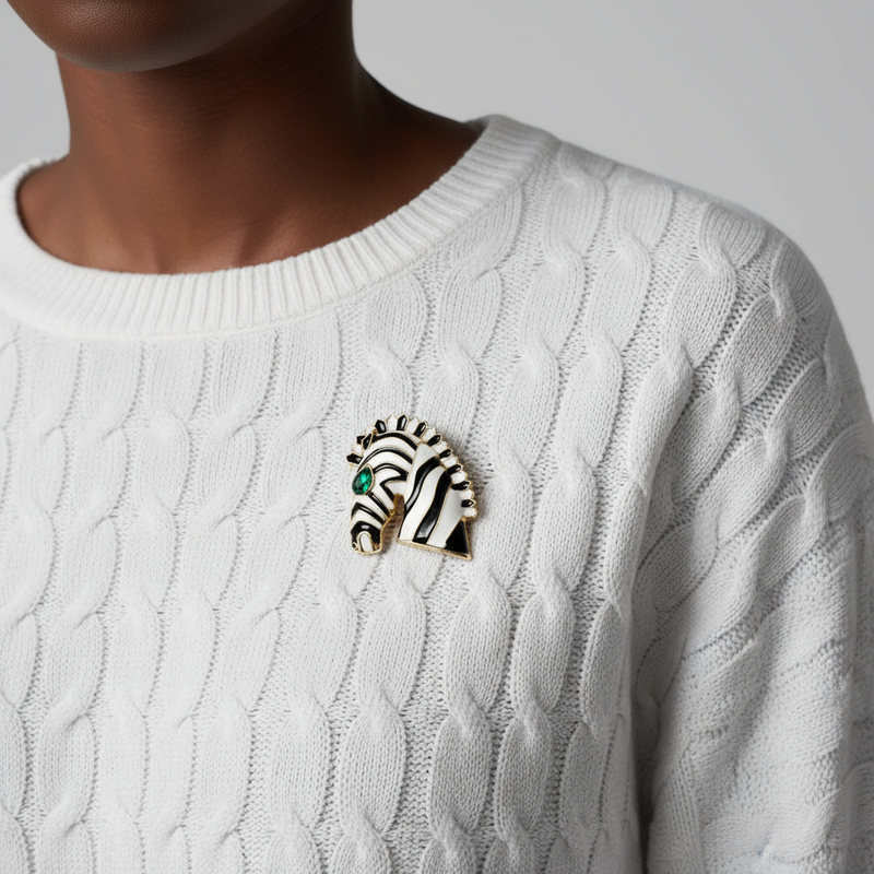 Elegant enamel zebra brooch with black and white stripes, gold-plated details, and a striking emerald-green gemstone eye, perfect for adding a touch of luxury and boldness to any outfit.