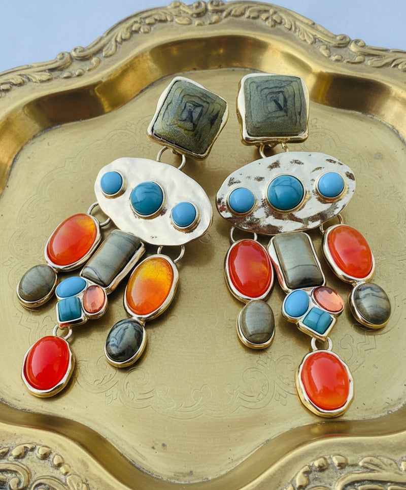 Colorful dangle earrings with gold backing, featuring orange, turquoise, and olive-green stones in various shapes and sizes arranged in a cascading design.