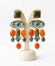 Colorful earrings with turquoise, orange, and green stones on a white stand.