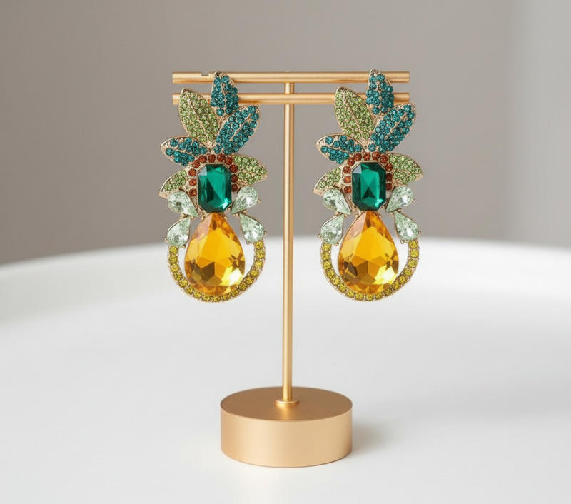 Pair of ornate earrings with green and yellow gemstones on a gold stand against a neutral background.