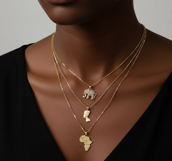 Gold necklaces with elephant and Africa map pendants on a model against a neutral background