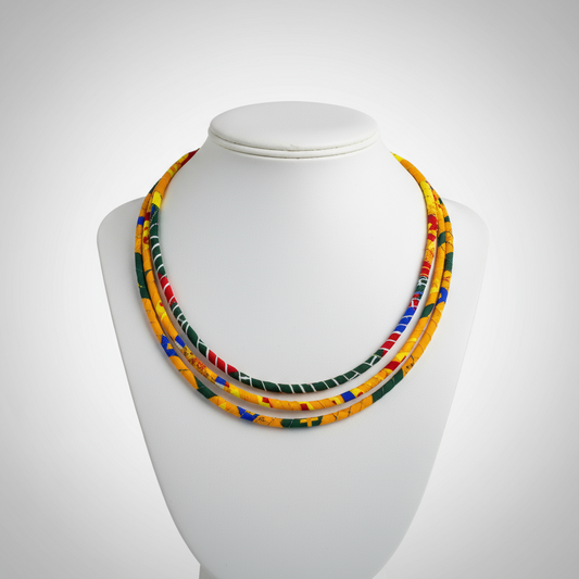 Ankara fabric-wrapped triple-strand necklace in bold red, yellow, green, and blue with matching round African print button earrings displayed on a black bust stand.