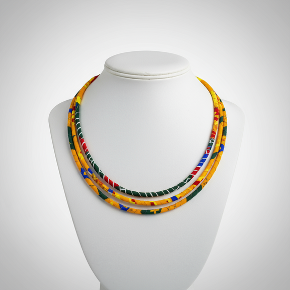 Ankara fabric-wrapped triple-strand necklace in bold red, yellow, green, and blue with matching round African print button earrings displayed on a black bust stand.