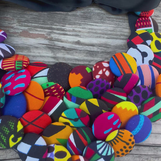 Colorful African print button necklace with satin ribbon tie, laid on rustic wood background.
