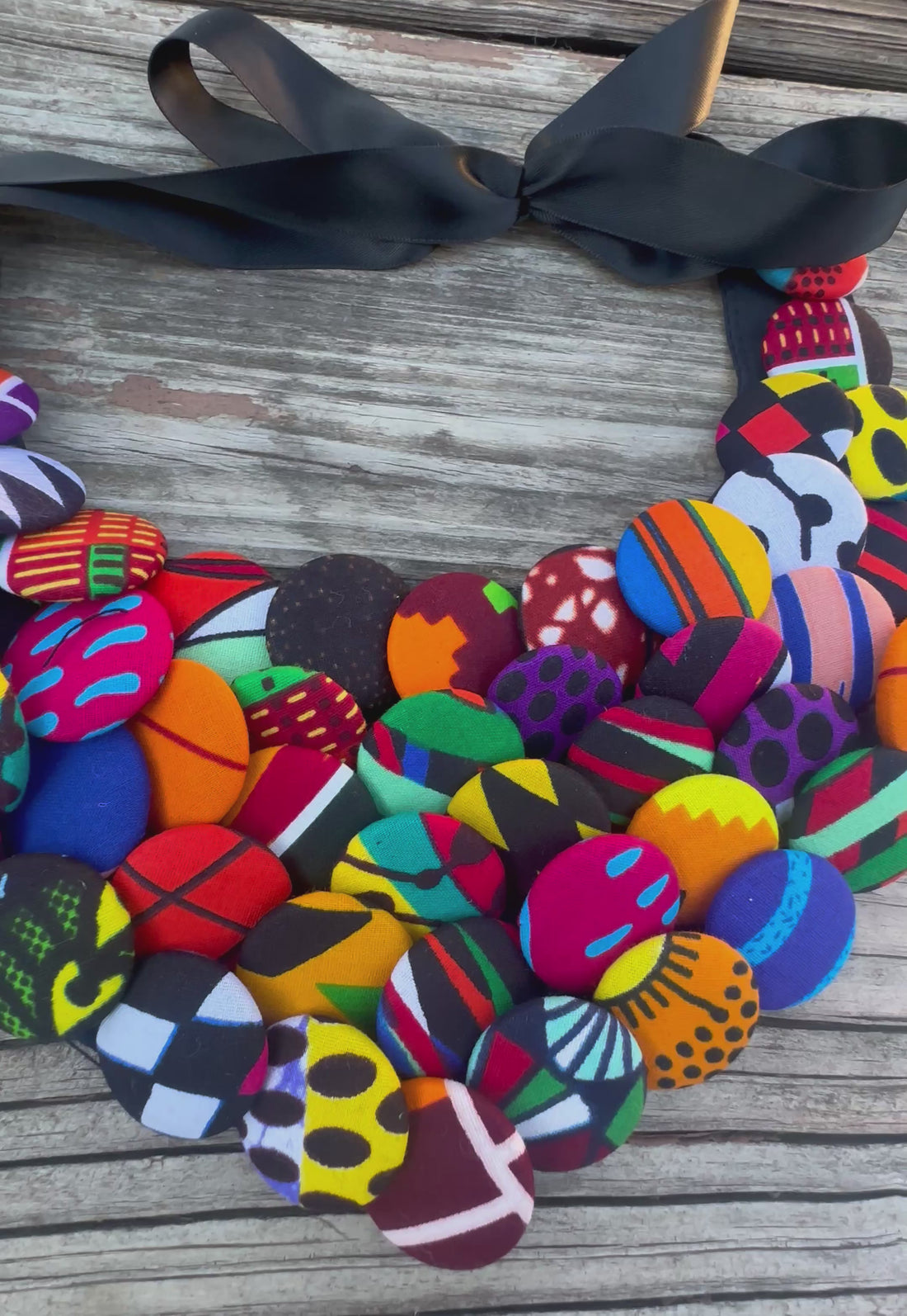 Colorful African print button necklace with satin ribbon tie, laid on rustic wood background.
