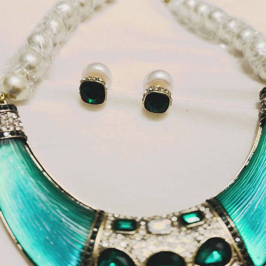Bold green gemstone and pearl statement necklace with crystal detailing and crescent-shaped collar on vintage tray