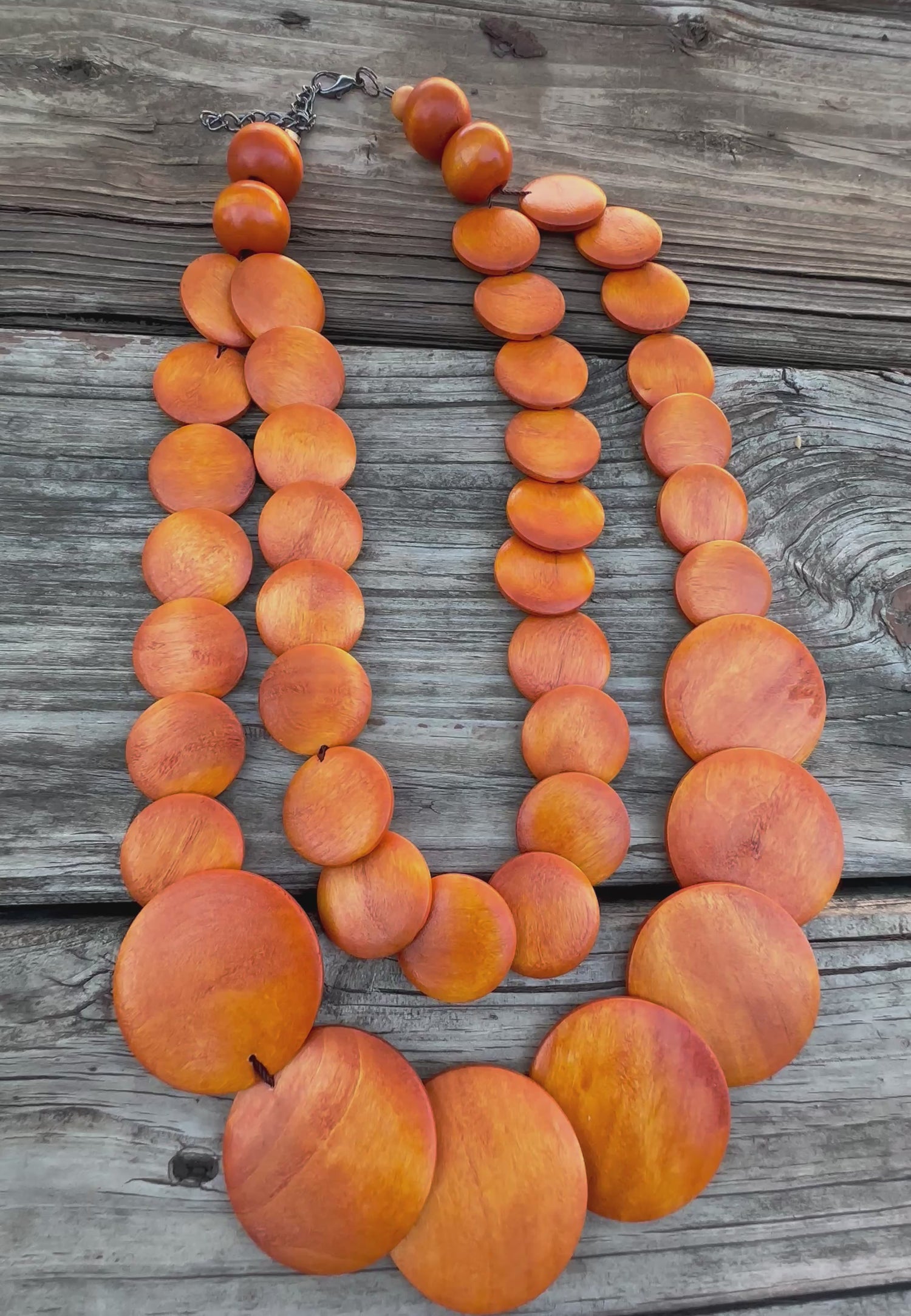 Double-strand orange wooden bead necklace with circular discs, displayed on rustic wooden background.
