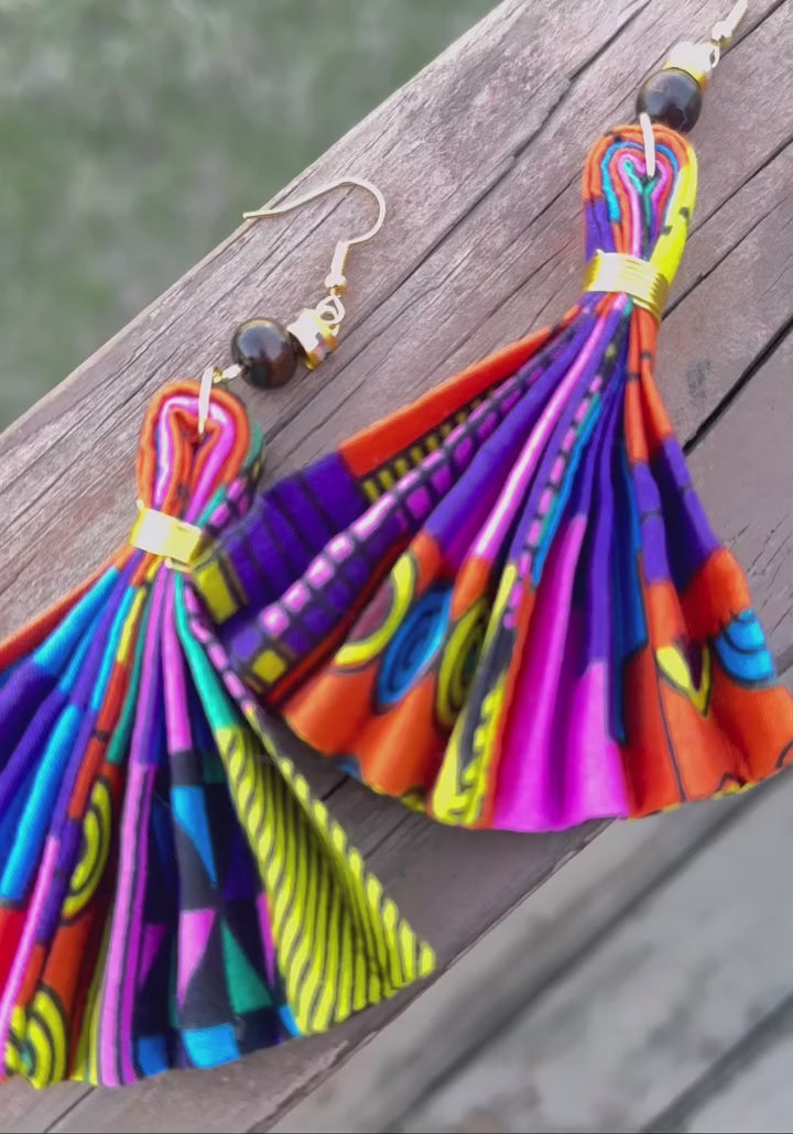 Gold hoop earrings with multicolor enamel stripes, displayed on a book page with pink roses in the background.